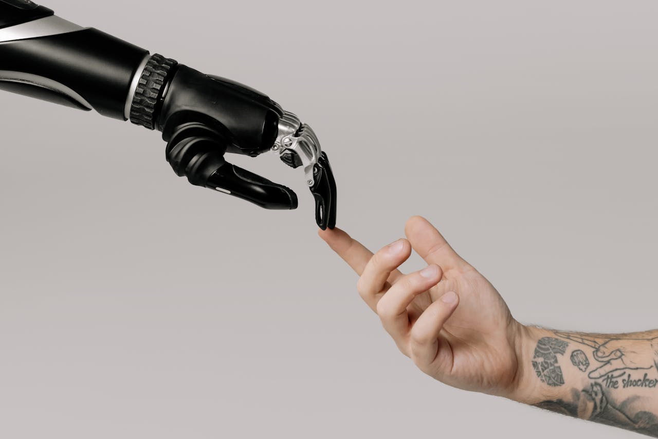 creative-02 A human hand with tattoos reaching out to a robotic hand on a white background.